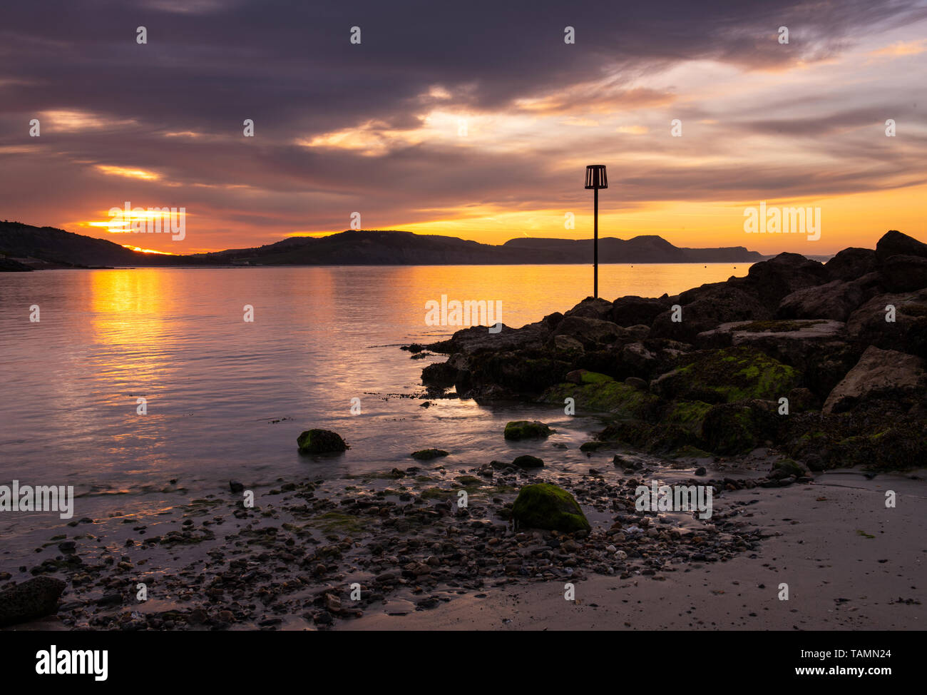 Lyme Regis, Dorset, Regno Unito. 27 Maggio, 2019. Regno Unito: Meteo gloriosi colori sunrise si riflettono nel mare calmo a Lyme Regis sulla fine Maggio Bank Holiday. Il mare si illumina come il sole sorge oltre la Jurassic Coast. Credito: Celia McMahon/Alamy Live News Foto Stock