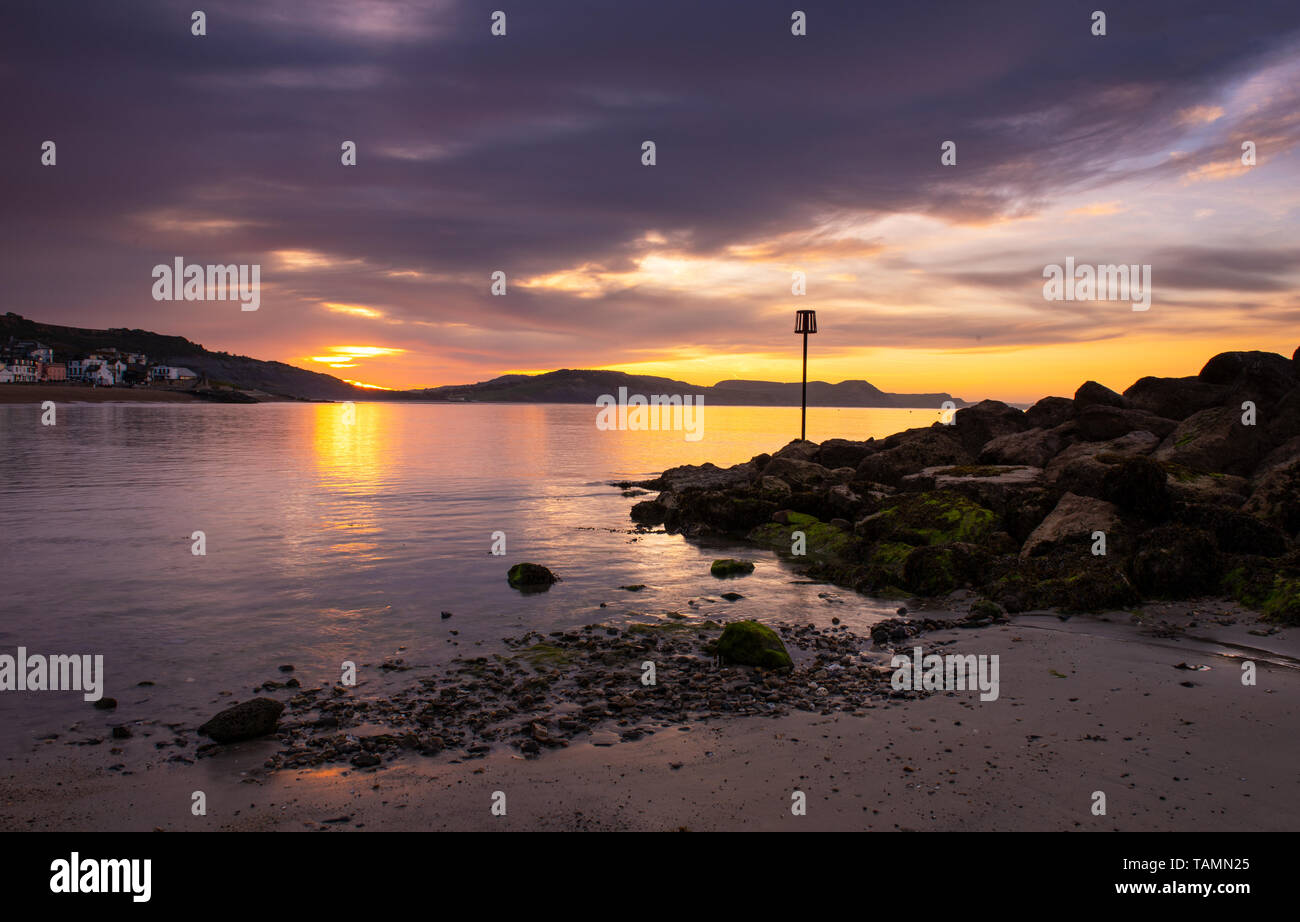 Lyme Regis, Dorset, Regno Unito. 27 Maggio, 2019. Regno Unito: Meteo gloriosi colori sunrise si riflettono nel mare calmo a Lyme Regis sulla fine Maggio Bank Holiday. Il mare si illumina come il sole sorge oltre la Jurassic Coast. Credito: Celia McMahon/Alamy Live News Foto Stock
