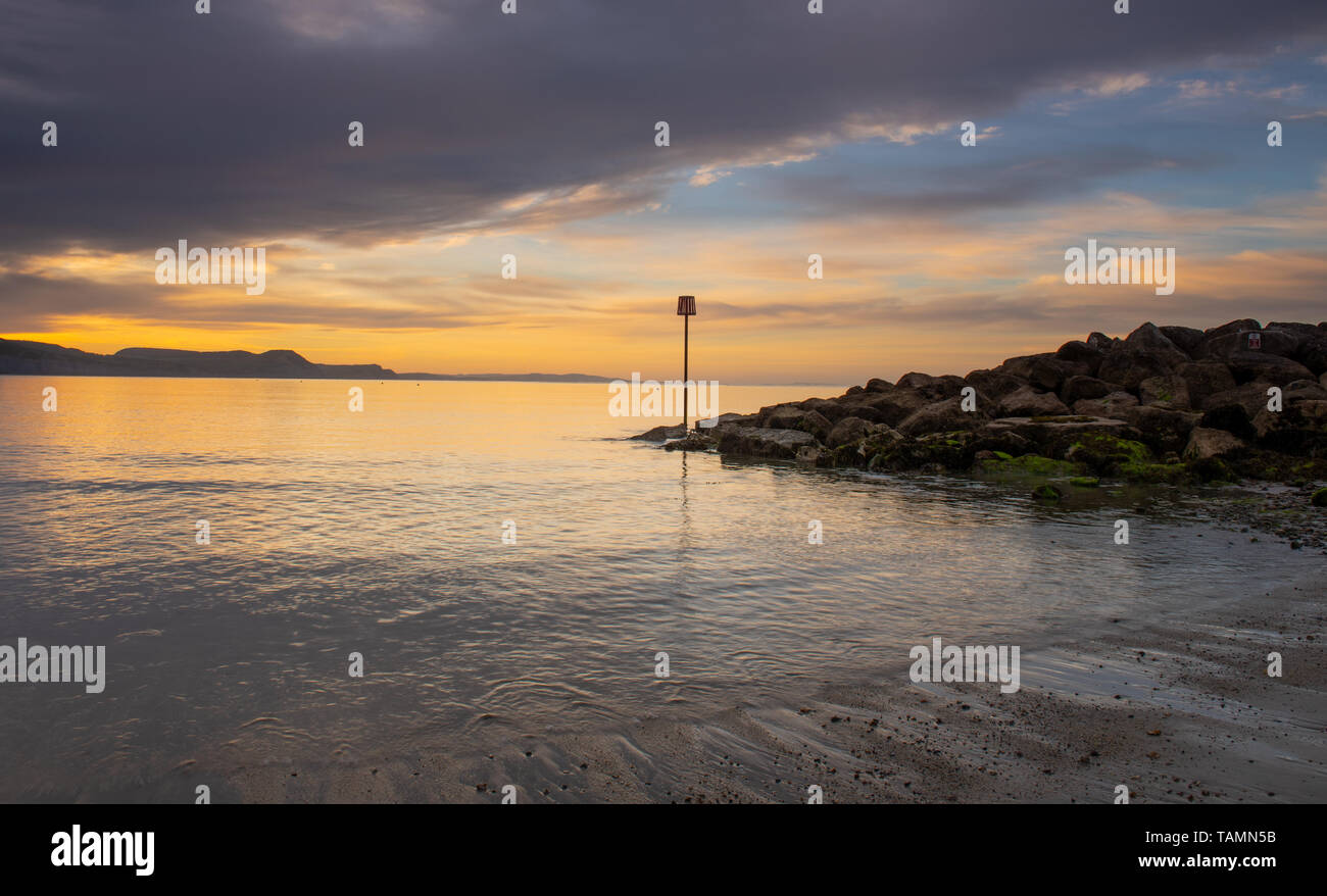 Lyme Regis, Dorset, Regno Unito. 27 Maggio, 2019. Regno Unito: Meteo gloriosi colori sunrise si riflettono nel mare calmo a Lyme Regis sulla fine Maggio Bank Holiday. Il mare si illumina come il sole sorge oltre la Jurassic Coast. Credito: Celia McMahon/Alamy Live News Foto Stock