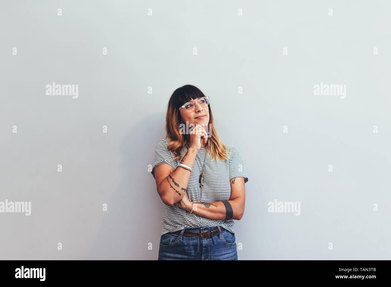 Ritratto di una imprenditrice in piedi contro un muro pensando a una soluzione. In prossimità di una donna in piedi con la mano sul mento e guardando lontano. Foto Stock