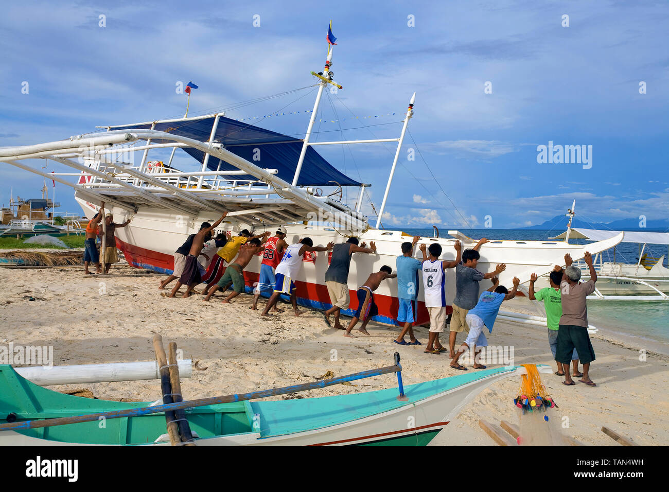 I pescatori spingendo una tradizionale barca da pesca dopo maintanance dalla spiaggia e l'oceano, Bounty beach, Malapascua island, Cebu, Filippine Foto Stock