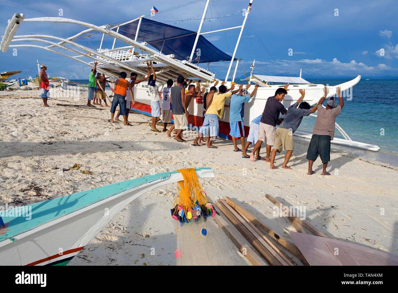 I pescatori spingendo una tradizionale barca da pesca dopo maintanance dalla spiaggia e l'oceano, Bounty beach, Malapascua island, Cebu, Filippine Foto Stock