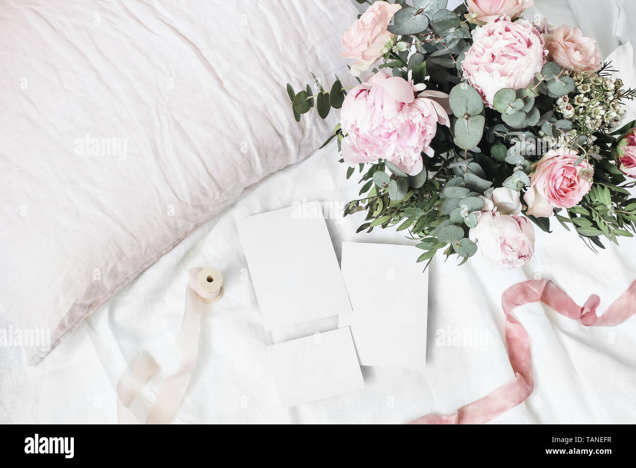 Accogliente camera da letto ancora vita scena. Matrimoni, compleanni bouquet di rose rosa peonia, fiori e rami di eucalipto. Nastri di seta su lino Biancheria da letto. Vuoto Foto Stock