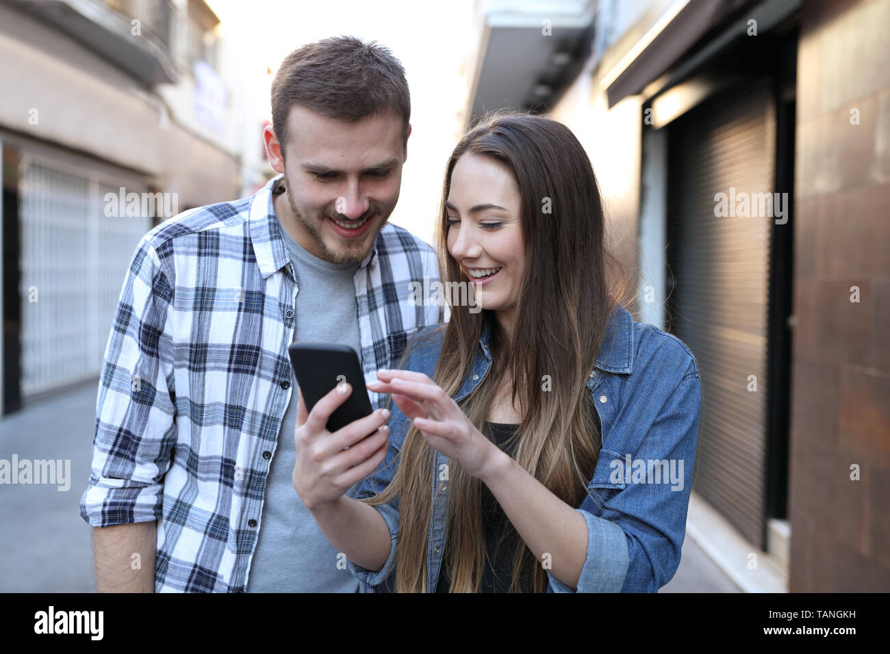 Vista frontale di due amici smart di esplorazione del contenuto del telefono a piedi in strada Foto Stock
