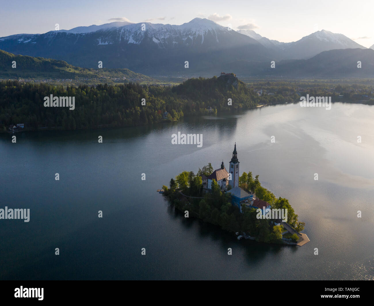 Sunrise vista aerea di St Marys chiesa sull isola del lago di Bled, Slovenia. Sullo sfondo vi è il castello di Bled su rocce e montagne distanti all'inizio su Foto Stock