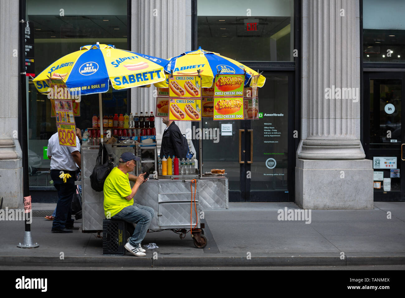 Venditore di street food che lavora a un chiosco di hot dog sotto ombrelli colorati a Manhattan, New York City, New York, USA. Foto Stock