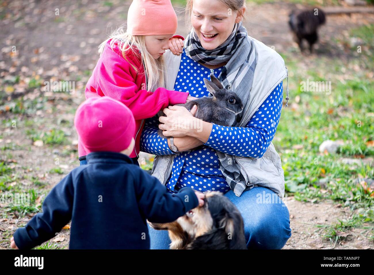 La mamma gioca con i suoi bambini e alimenta gli animali domestici nel cortile della fattoria Foto Stock