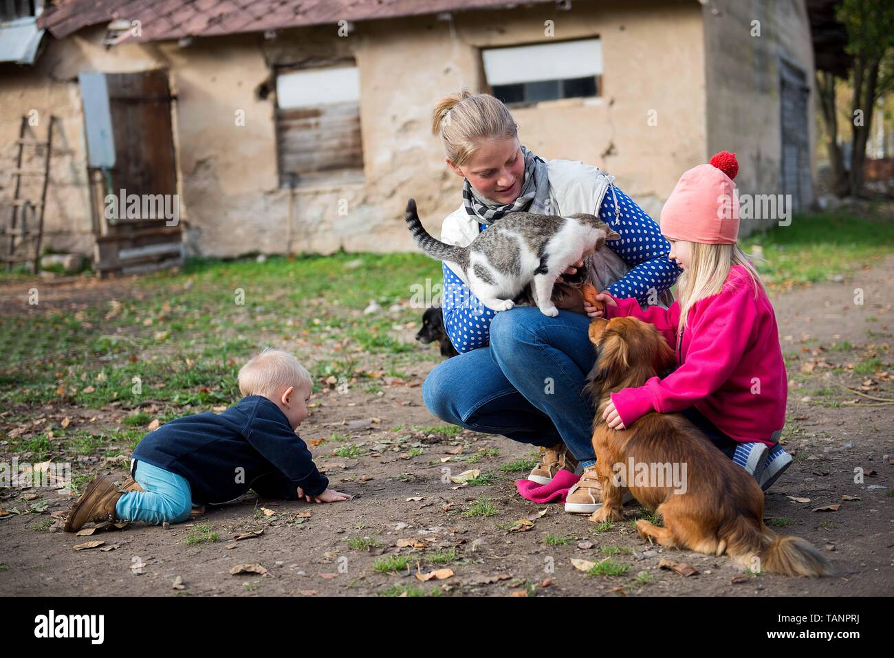 La mamma gioca con i suoi bambini e alimenta gli animali domestici nel cortile della fattoria Foto Stock
