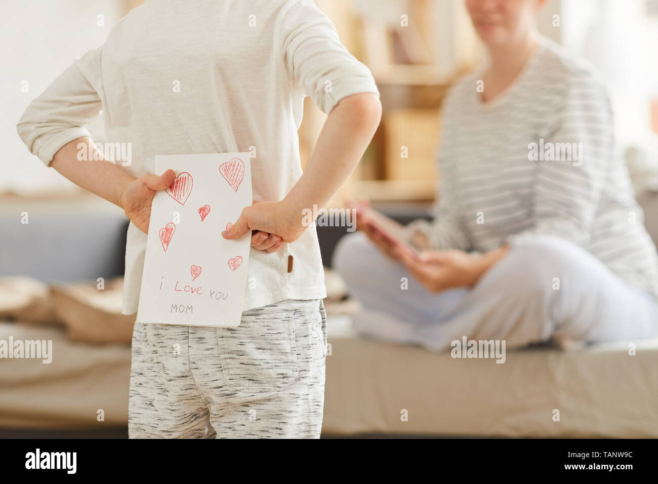 Close-up di un irriconoscibile boy in - homewear nascondendo biglietto di auguri per la madre alle spalle indietro mentre si effettua la sorpresa in mattinata Foto Stock
