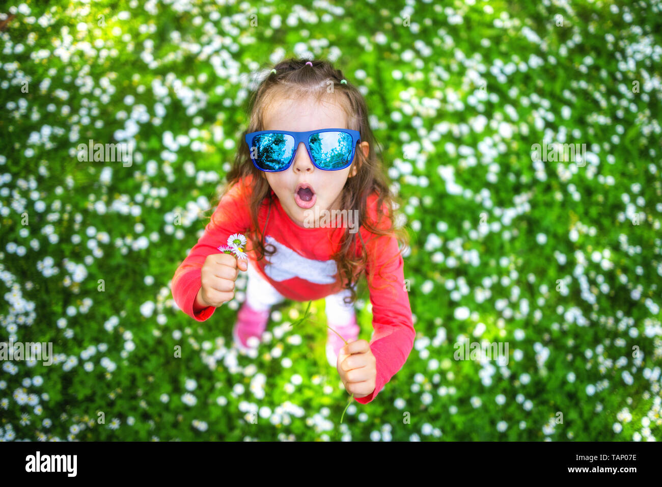 Felice sorridente bambina con capelli ricci tra il campo a margherita. Foto Stock