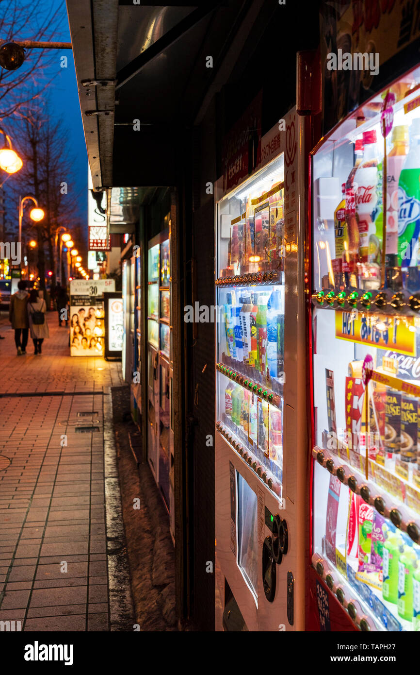 Vista lungo la fila di giapponese di soft drink distributori automatici sulla strada di notte tempo nella città di Kumamoto, Giappone. Foto Stock