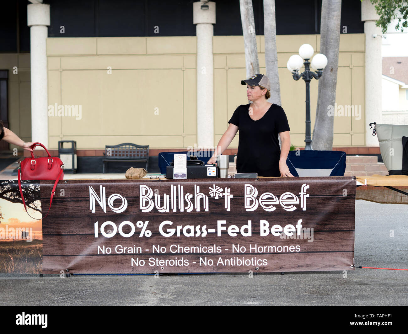 La donna sta a tavola con un banner pubblicitario 100 % grass fed-carni bovine al Corpus Christi Southside mercato agricolo. Il Corpus Christi, Texas USA. Foto Stock