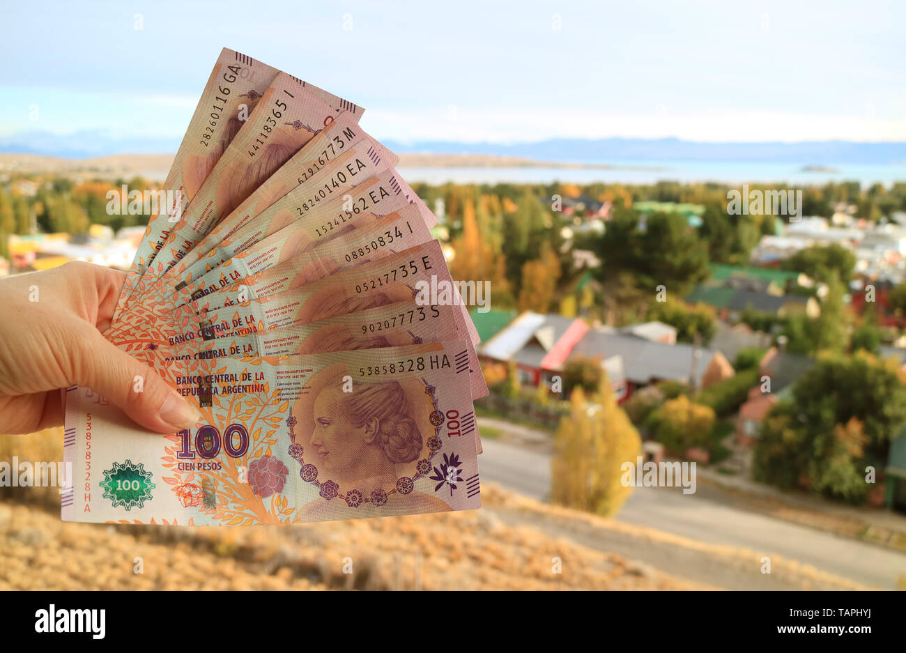 Donna di mano azienda mazzetto argentino di 100 Pesos banconote (anteriore) con sfocata EL Calafate città in background Foto Stock