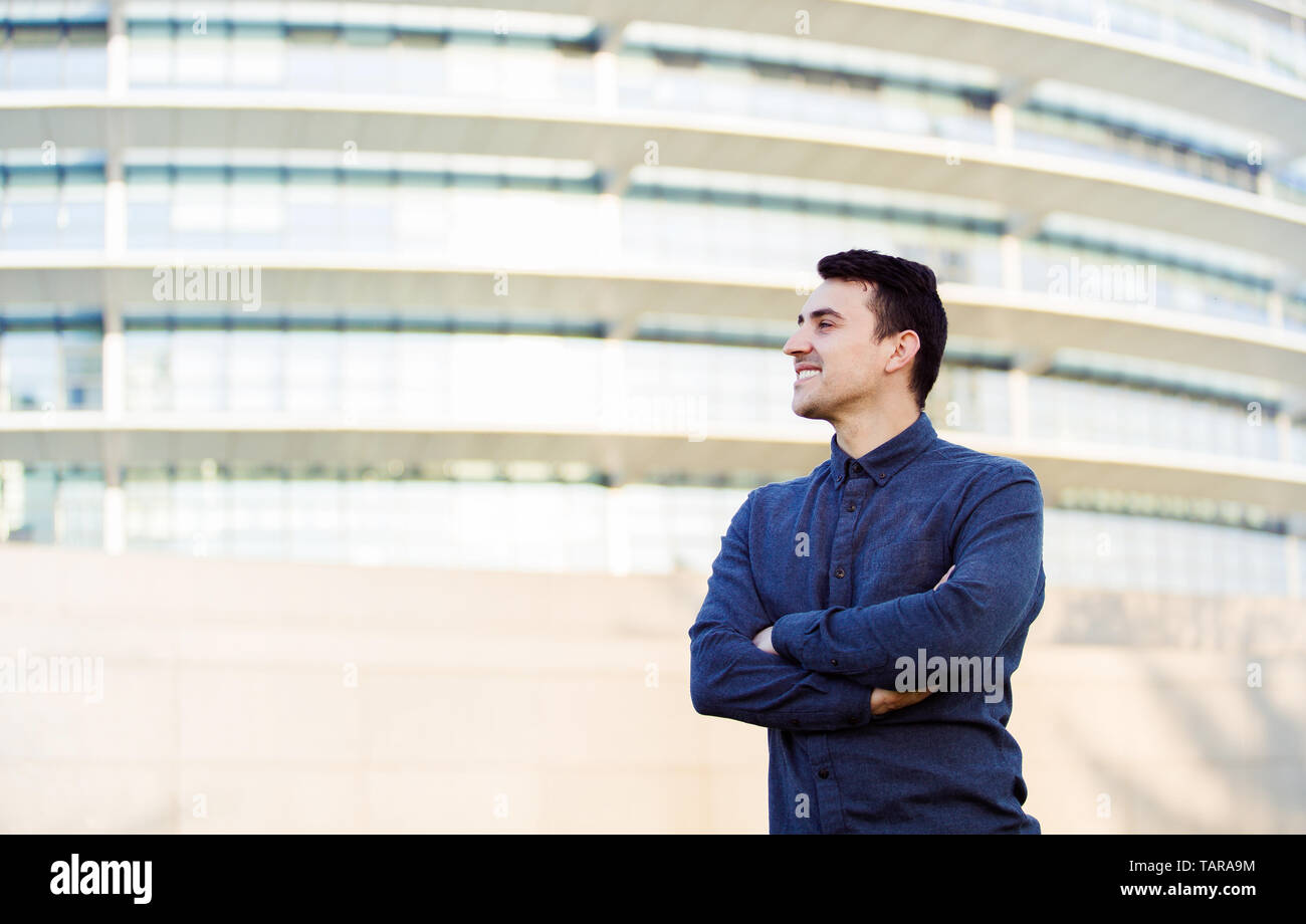 Certi imprenditori uomo giovane impreditore ritratto contro ufficio edificio dello sfondo. Sorridente maschio caucasico professional in smart casual Foto Stock