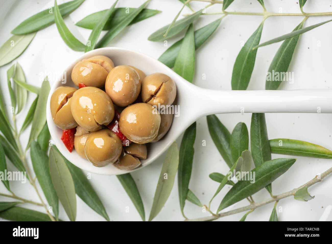 Olive speziate sul cucchiaio bianco e lo sfondo di legno. Le tapas spagnole Foto Stock
