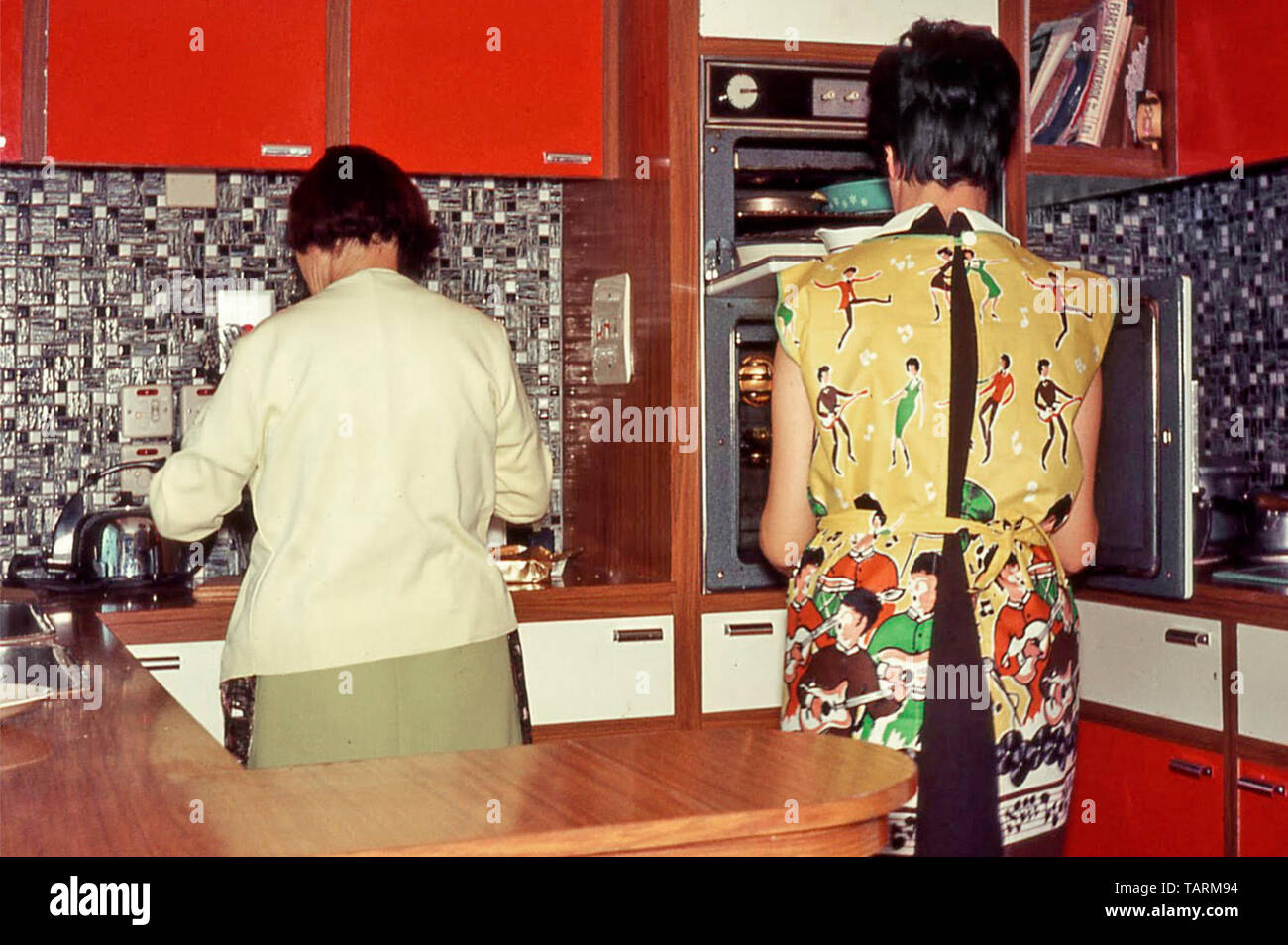 Archival vista posteriore del giovane massaia a forno & la mamma di preparare il cibo nel nuovo 1966 cucina DIY interni piani Formica madre e figlia England Regno Unito Foto Stock