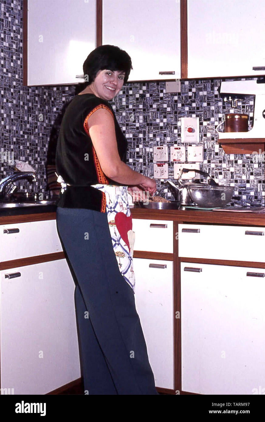 Vista Archiviazione dei giovani casalinga che prepara il cibo nel nuovo 1968 cucina DIY interno con piani di lavoro di Formica mosaico Piastrellatura murale & food mixer England Regno Unito Foto Stock