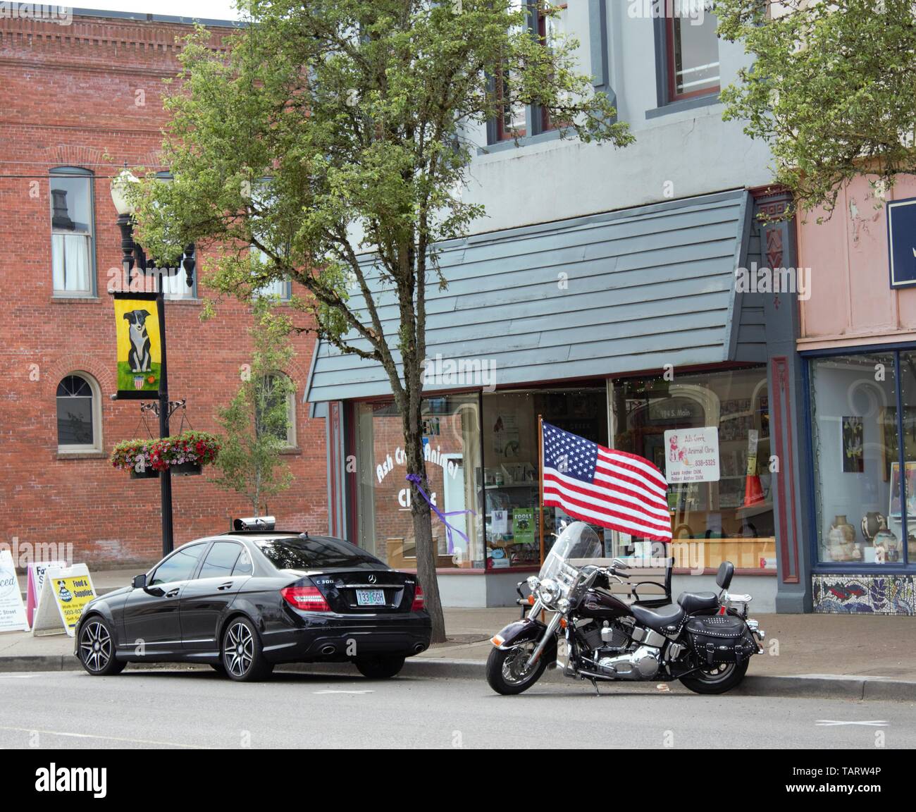 Una bandiera americana è lo sfondo di questo Harley Davidson Moto parcheggiata sulla strada di una piccola città di Oregon. Foto Stock