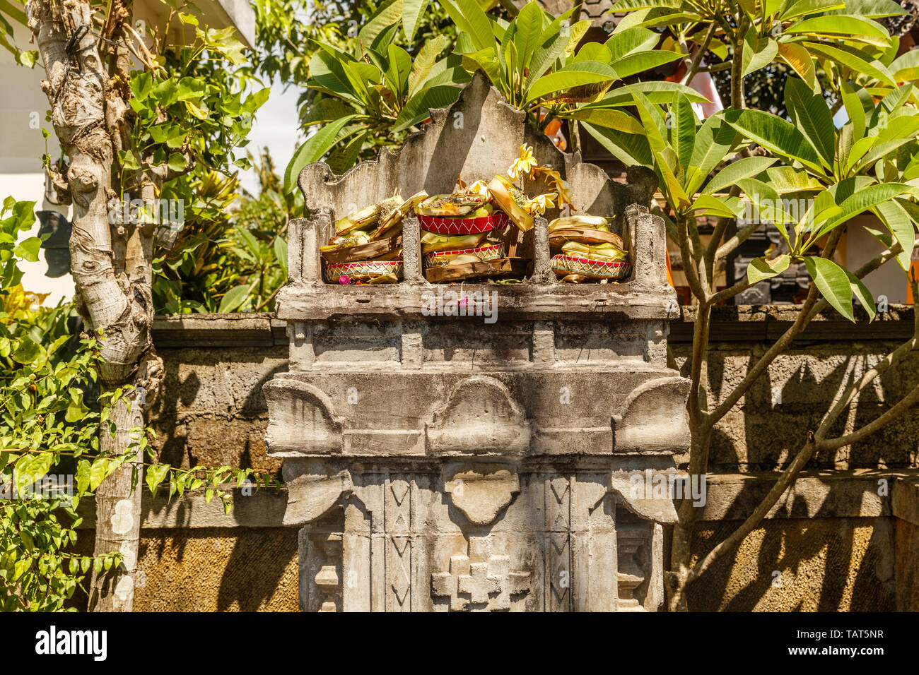 Tripla altare in pietra dedicato alla Trimurti - Brahma, Shiva e Vishnu con indù tradizionali offerte Balinese canang sari. Bali, Indonesia. Foto Stock