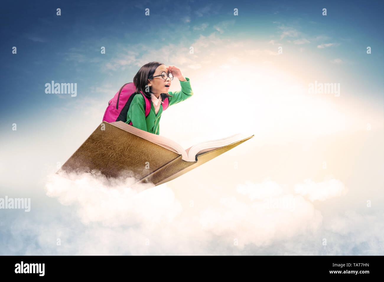Asiatica ragazza carina con gli occhiali e zainetto seduta sul libro con cielo blu sullo sfondo. Si torna a scuola concept Foto Stock