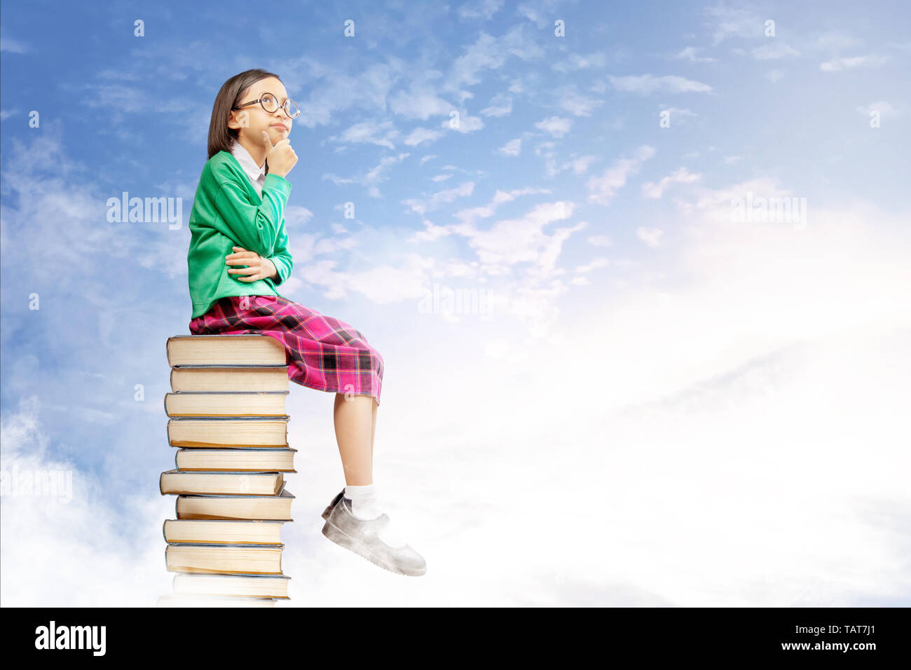 Asiatica ragazza carina con gli occhiali pensare mentre è seduto sulla pila di libri con cielo blu sullo sfondo. Si torna a scuola concept Foto Stock