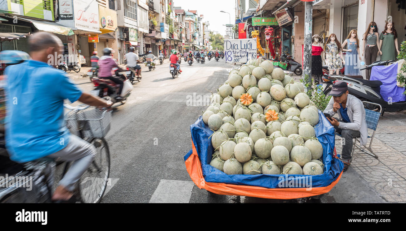 La città di Ho Chi Minh, Vietnam - Aprile 27, 2019: un carrello di meloni, una fila di manichini e dragon costumi per vendita lungo Tran Hung Dao Street. Foto Stock