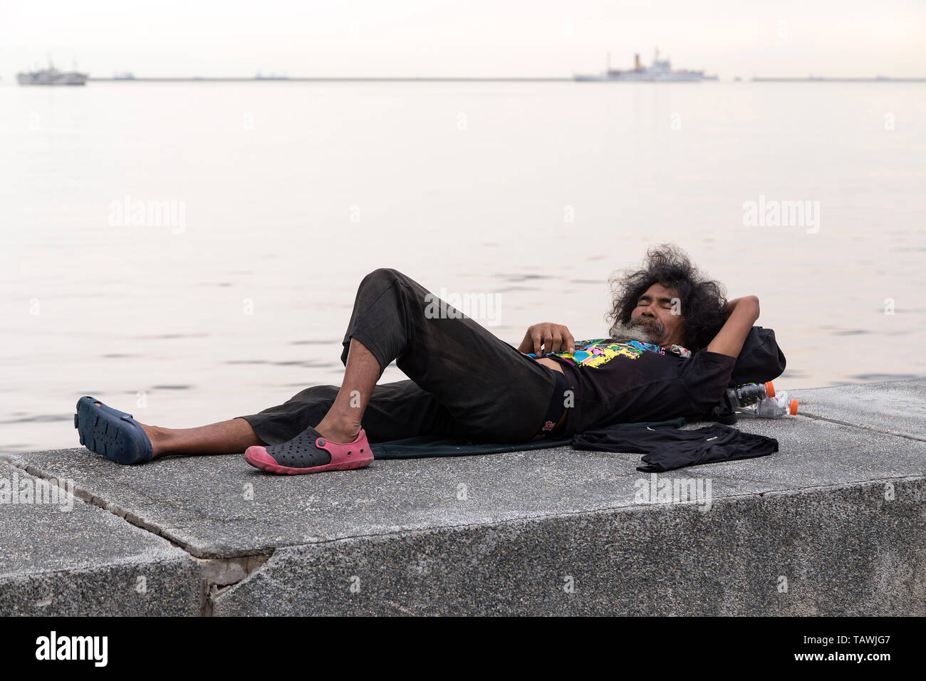 Manila, Filippine - 22 Giugno 2016: senzatetto uomo dorme in riva al mare Foto Stock