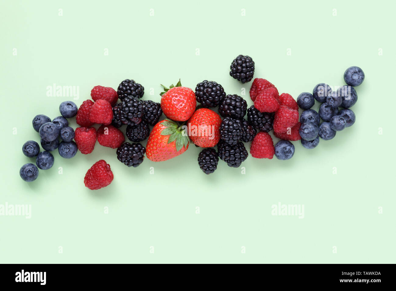 Fresco di frutti di bosco misti disposti in una linea sulla pianura sfondo verde Foto Stock