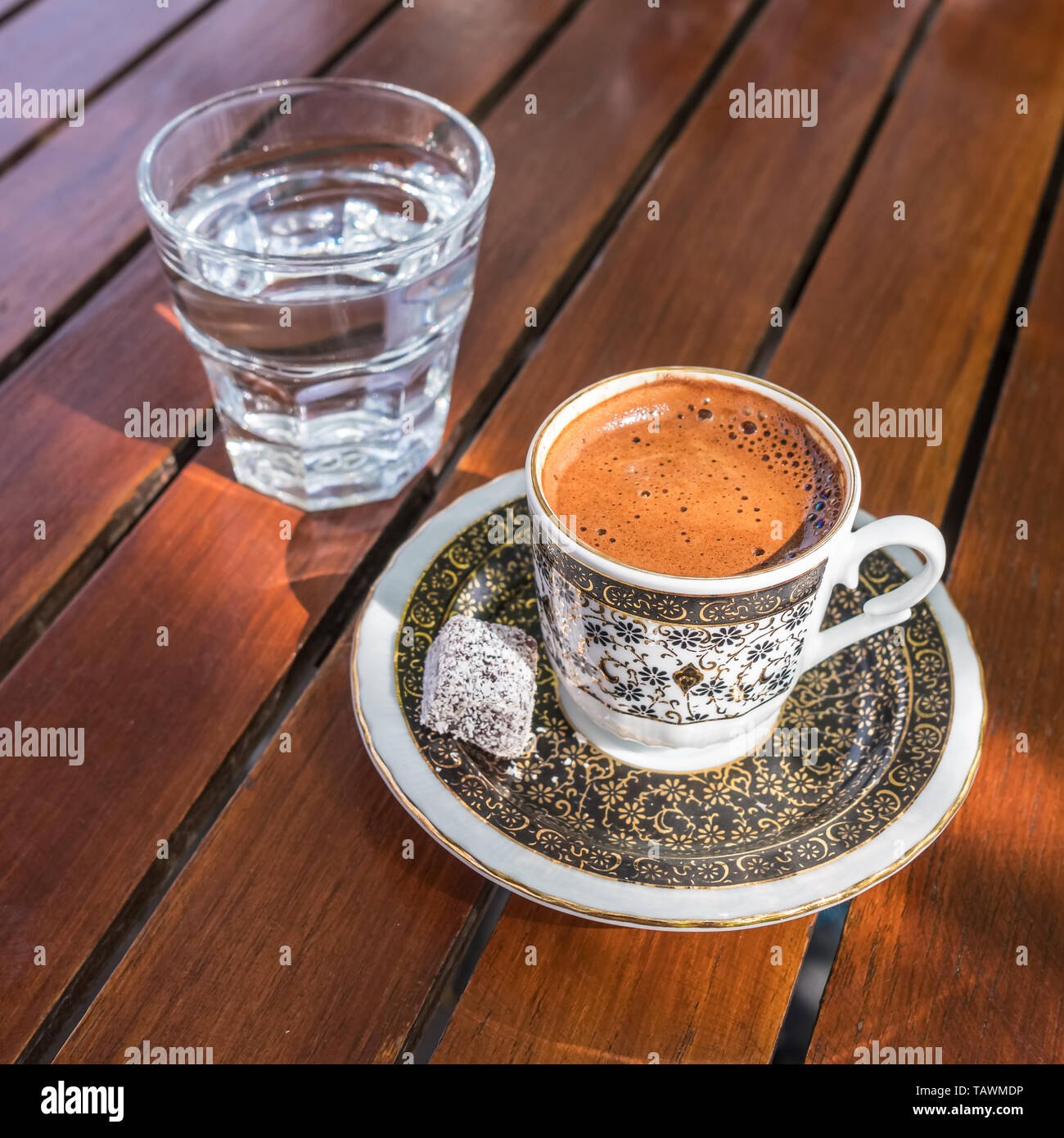 Forti tradizionali e scuro caffè turco servito con un bicchiere di acqua su un lato su una tavola di legno in outdoor cafe Foto Stock