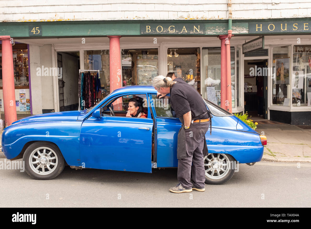 Blu classico Saab con passeggeri di fumare una sigaretta, High Street, Totnes, Devon, Regno Unito Foto Stock