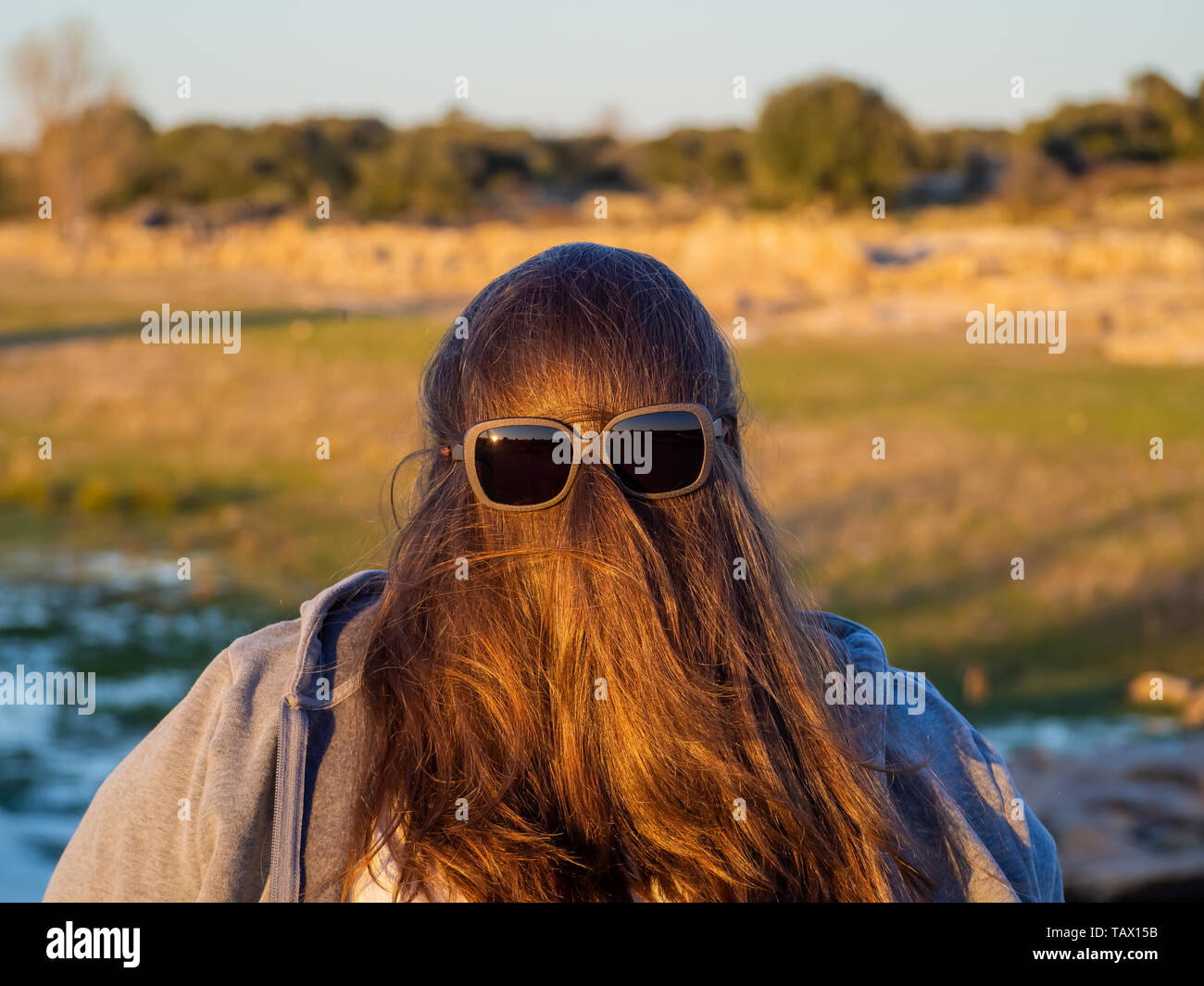 Una curva donna fare gesti divertenti con i capelli davanti al suo volto e occhiali da sole Foto Stock