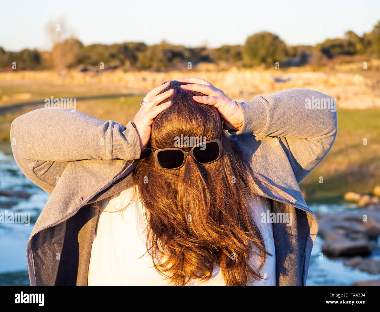 Una curva donna fare gesti divertenti con i capelli davanti al suo volto e occhiali da sole Foto Stock