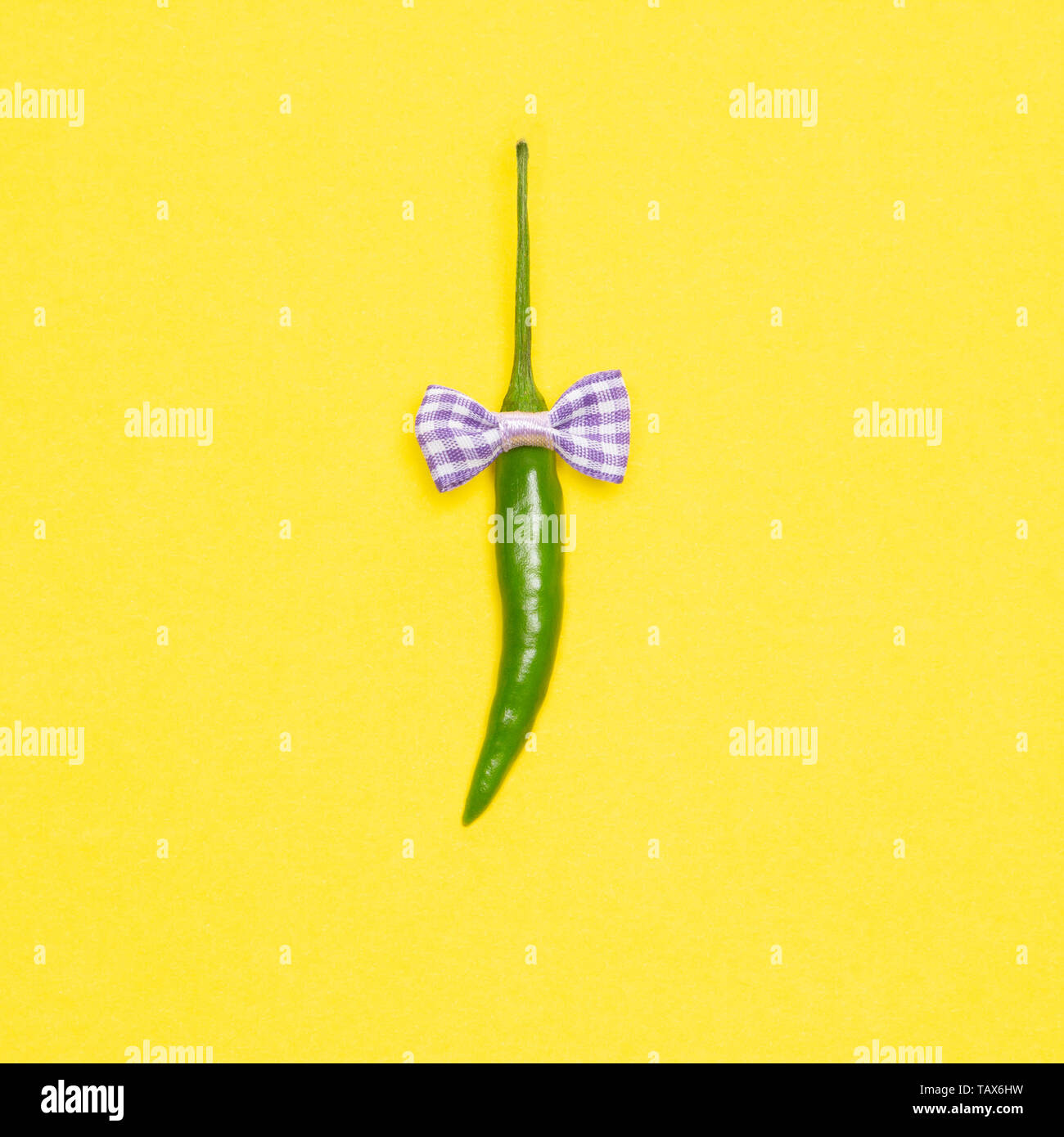 Peperoncino verde pepe con bow tie luminoso su sfondo giallo. Allegro concetto minimalista Foto Stock