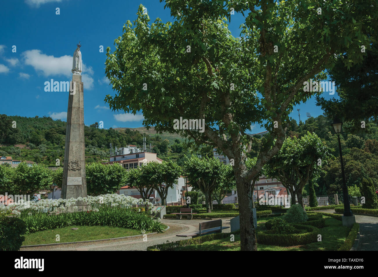 Statua in marmo della Madonna su pietra gogna presso il giardino fiorito in una giornata di sole a Seia. Un bel villaggio di Portogallo conosciuto anche per il suo delizioso formaggio. Foto Stock