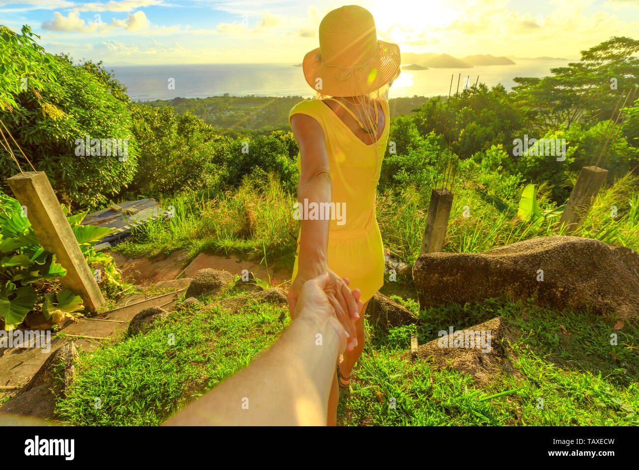 Follow me. Tourist donna in abito giallo tenendo la mano del partner a Seychelles, Oceano Indiano. Vedute spettacolari di Praslin da vista dall'alto di La Digue Foto Stock