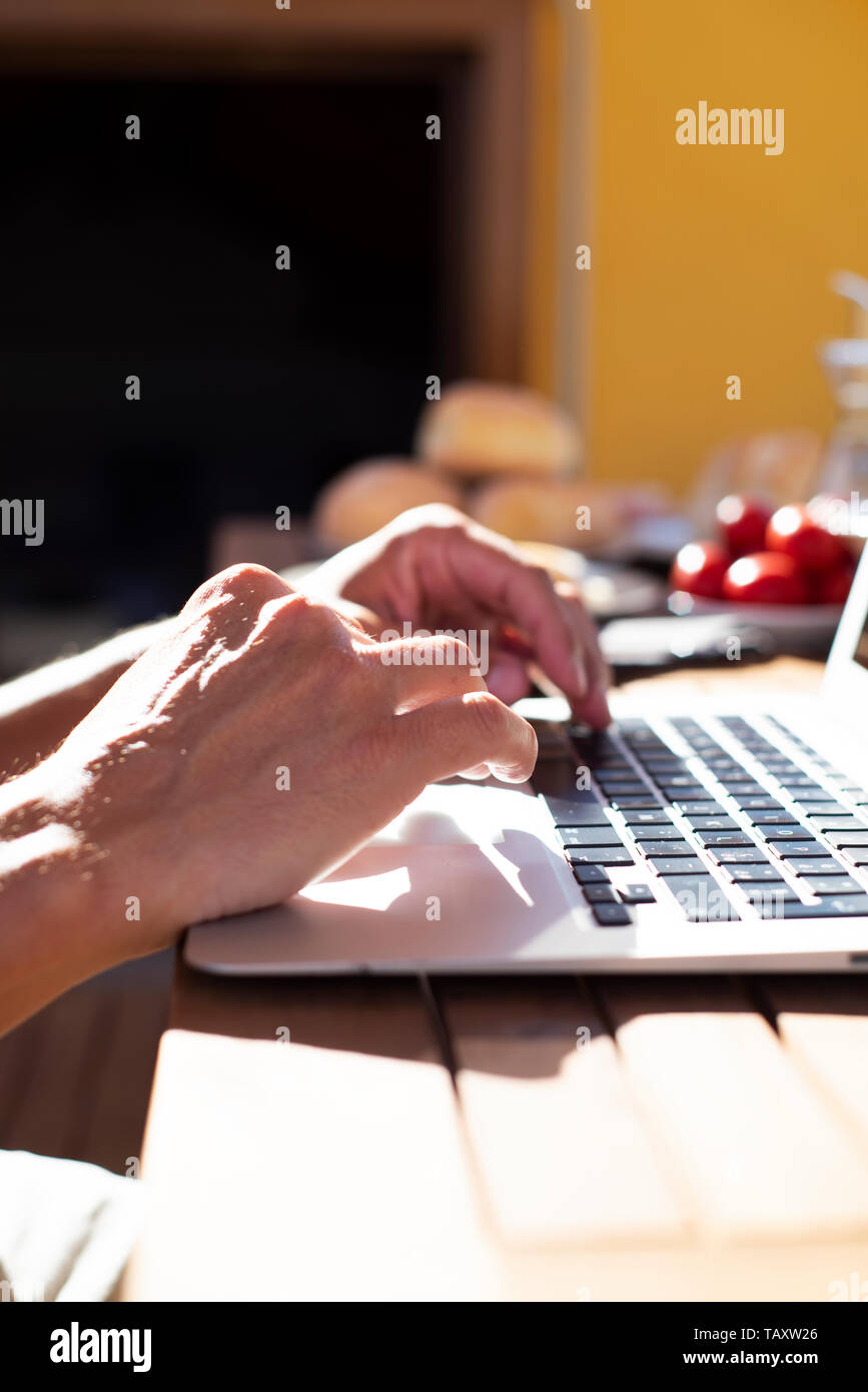 Primo piano di un giovane uomo caucasico usando un computer portatile seduti ad un tavolo di legno all'aperto durante un pasto Foto Stock
