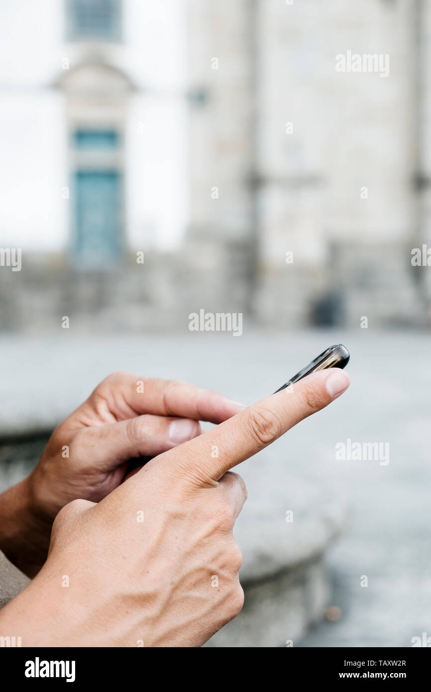 Primo piano di un giovane uomo caucasico usando il suo smpartphone sulla strada, nel centro storico di una città europea Foto Stock