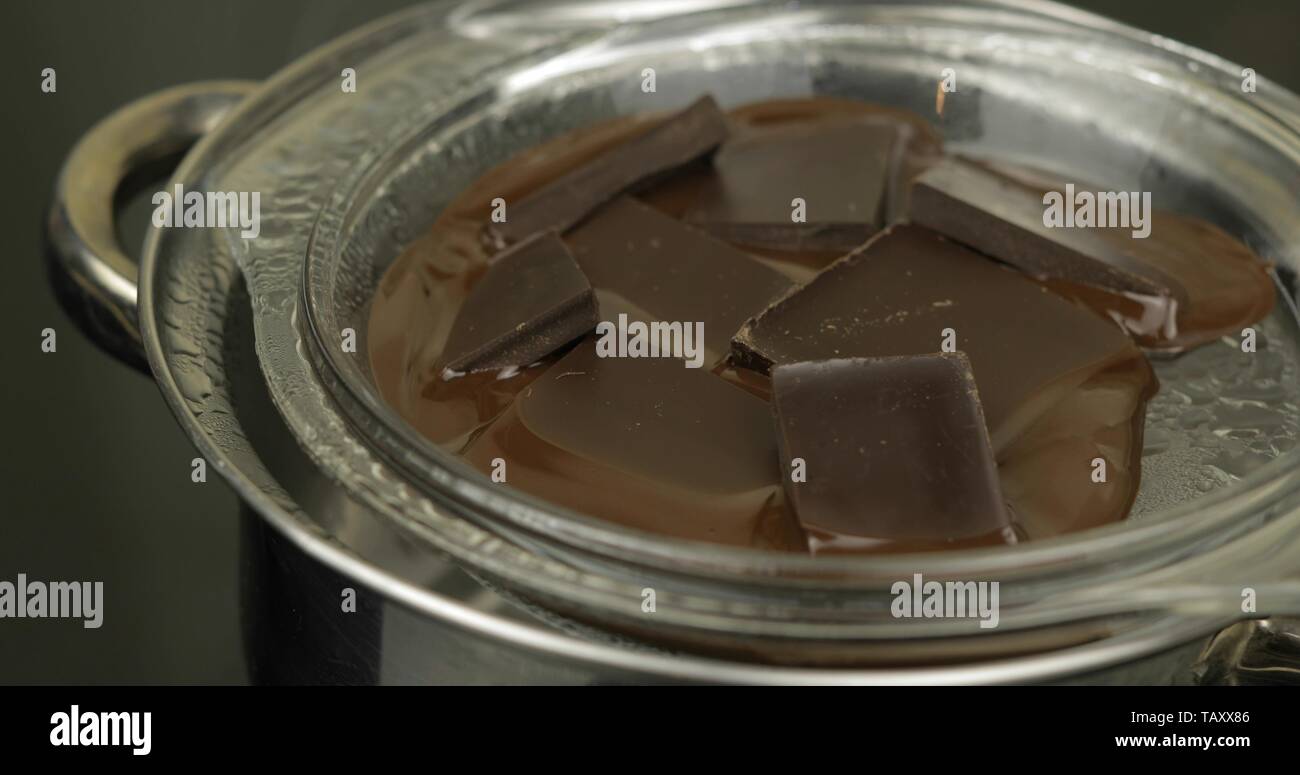 Fondere il cioccolato fondente in un recipiente su hot acqua bollita in pentola sulla stufa. Concetto di cioccolato fatte. Massa di fusione del cioccolato in una pentola. Close-up shot Foto Stock