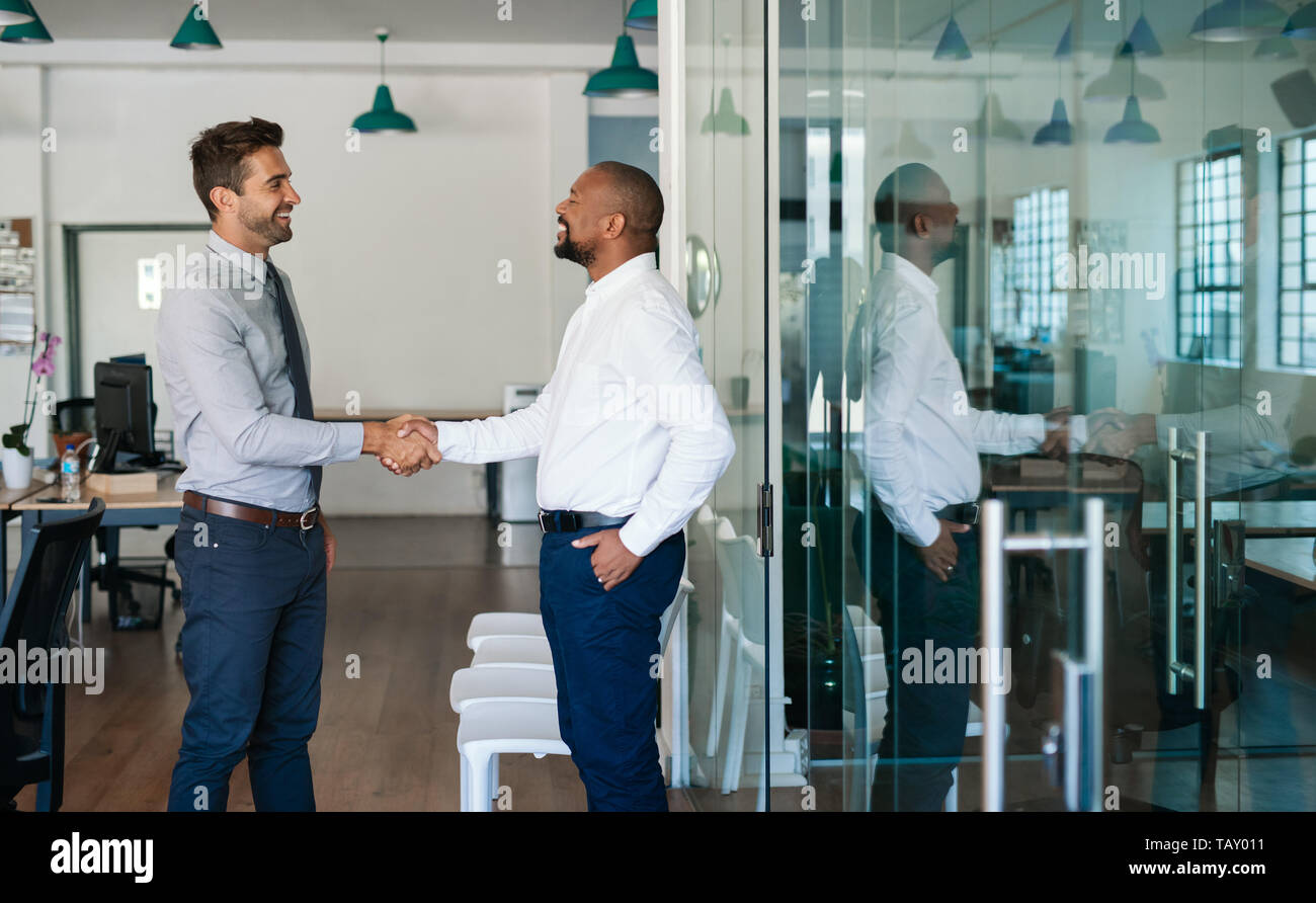 Due diversi imprenditori in piedi in un ufficio ridendo e agitando le mani insieme dopo una riunione di successo Foto Stock
