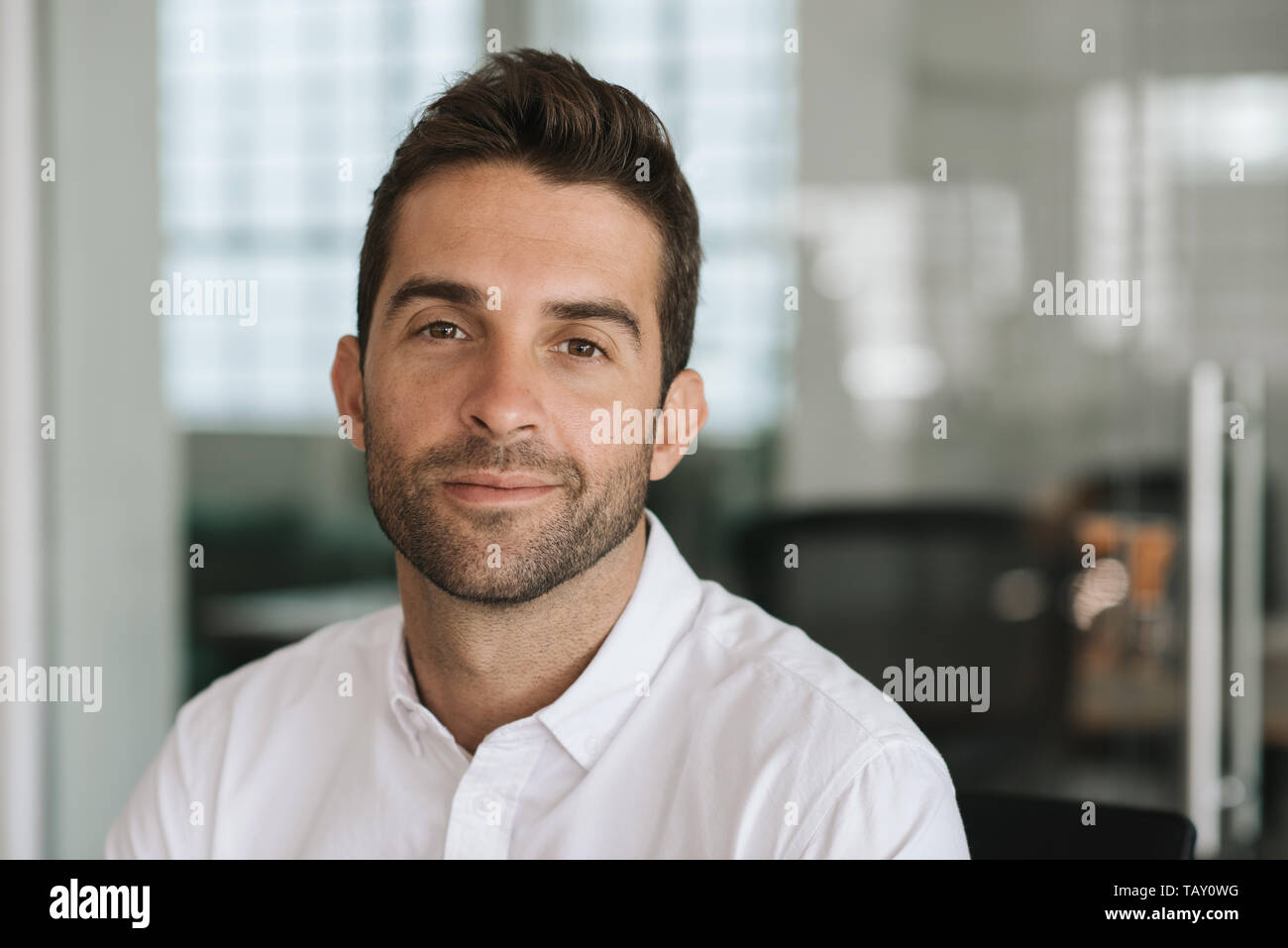 Ritratto di un giovane imprenditore sorridente con fiducia mentre è seduto da solo alla sua scrivania in un ufficio moderno Foto Stock