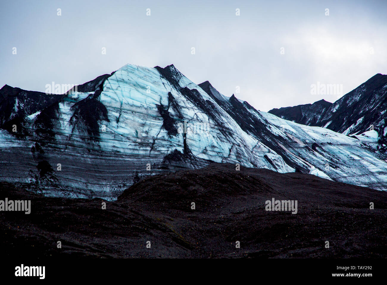 Impressionante blu-nero parete del ghiacciaio con sabbia di cenere in primo piano nel cielo grigio Foto Stock