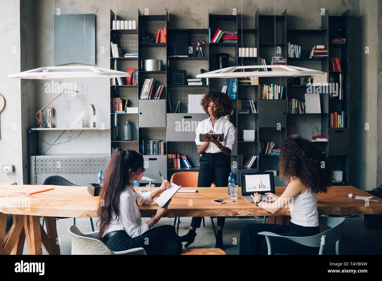 Tre giovani imprenditrici multiculturale avente una riunione informale in moderno spazio aperto- inventiva, interazione, dedizione Foto Stock