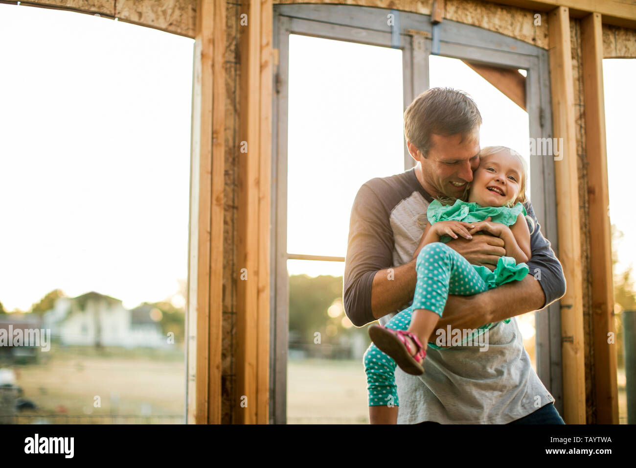 Padre sorridente scherzosamente solletica la sua giovane figlia presso il cantiere per la costruzione della loro nuova casa. Foto Stock