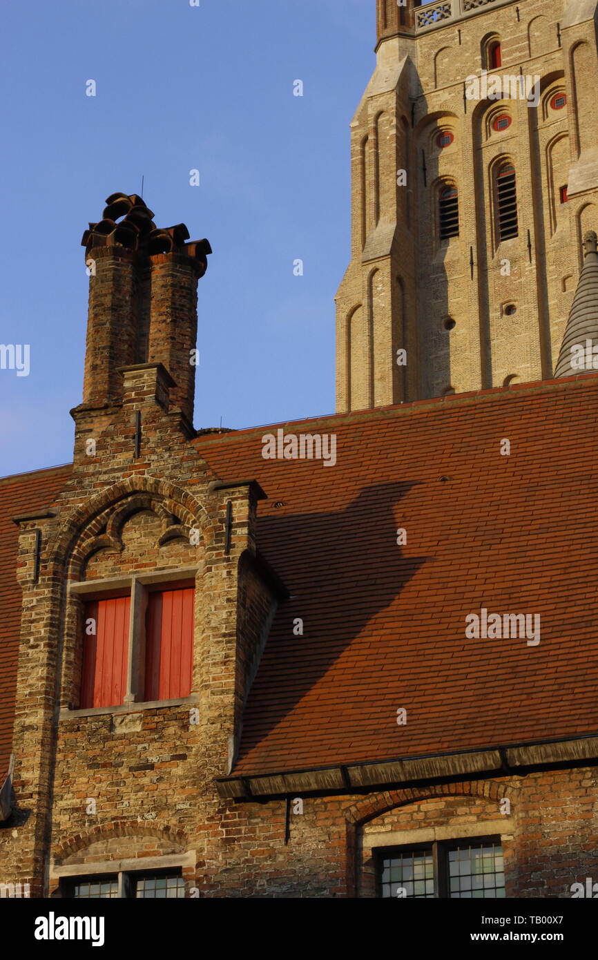 Costruzione di dettaglio nella città di Brugge che mostra un tetto dalle tegole rosse, camino e parte di una torre campanaria Foto Stock