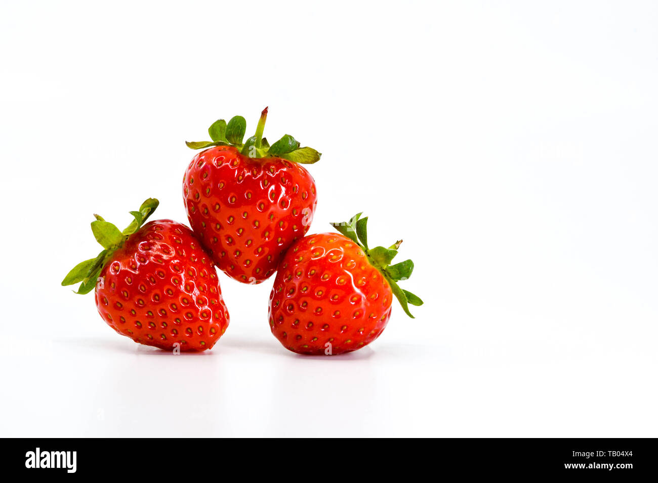 Chiudere fino a tre fragole mature equilibratura su ogni altra. Tutti sono isolate contro uno sfondo bianco con spazio per copiare sulla sinistra. Foto Stock