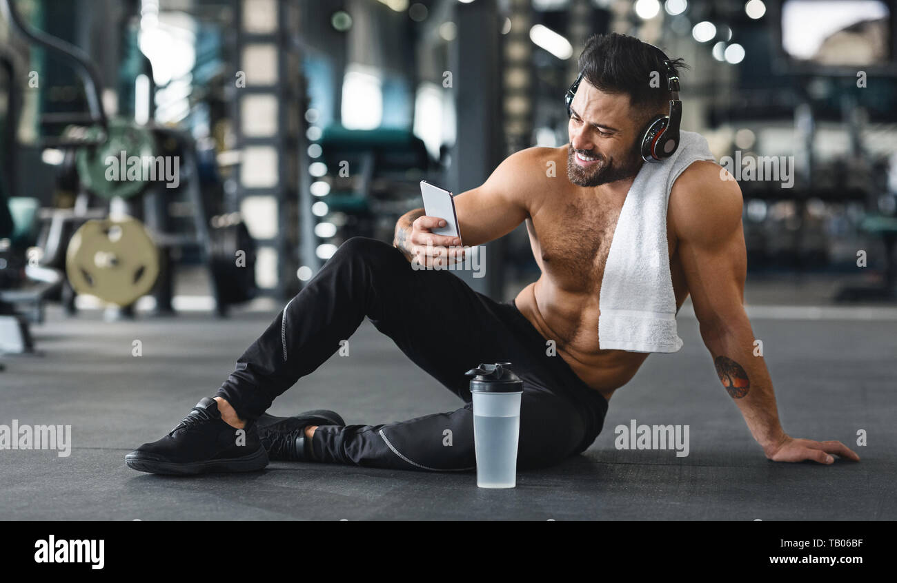 Uomo muscolare tramite cellulare in palestra, spazio libero Foto Stock