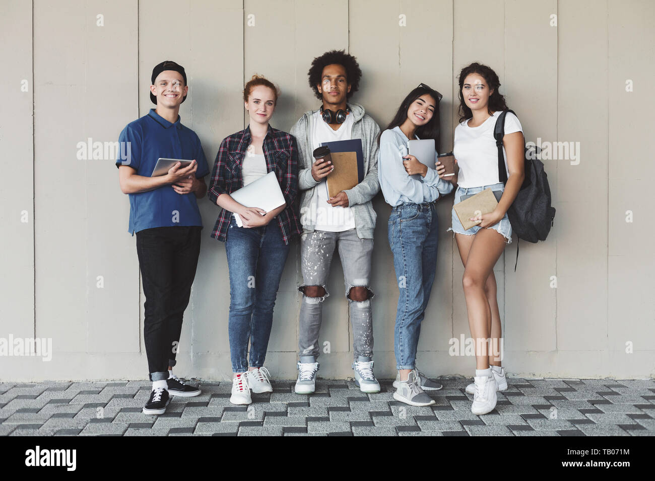 Felice studenti del college in posa con lo studio personale alla parete del campus Foto Stock