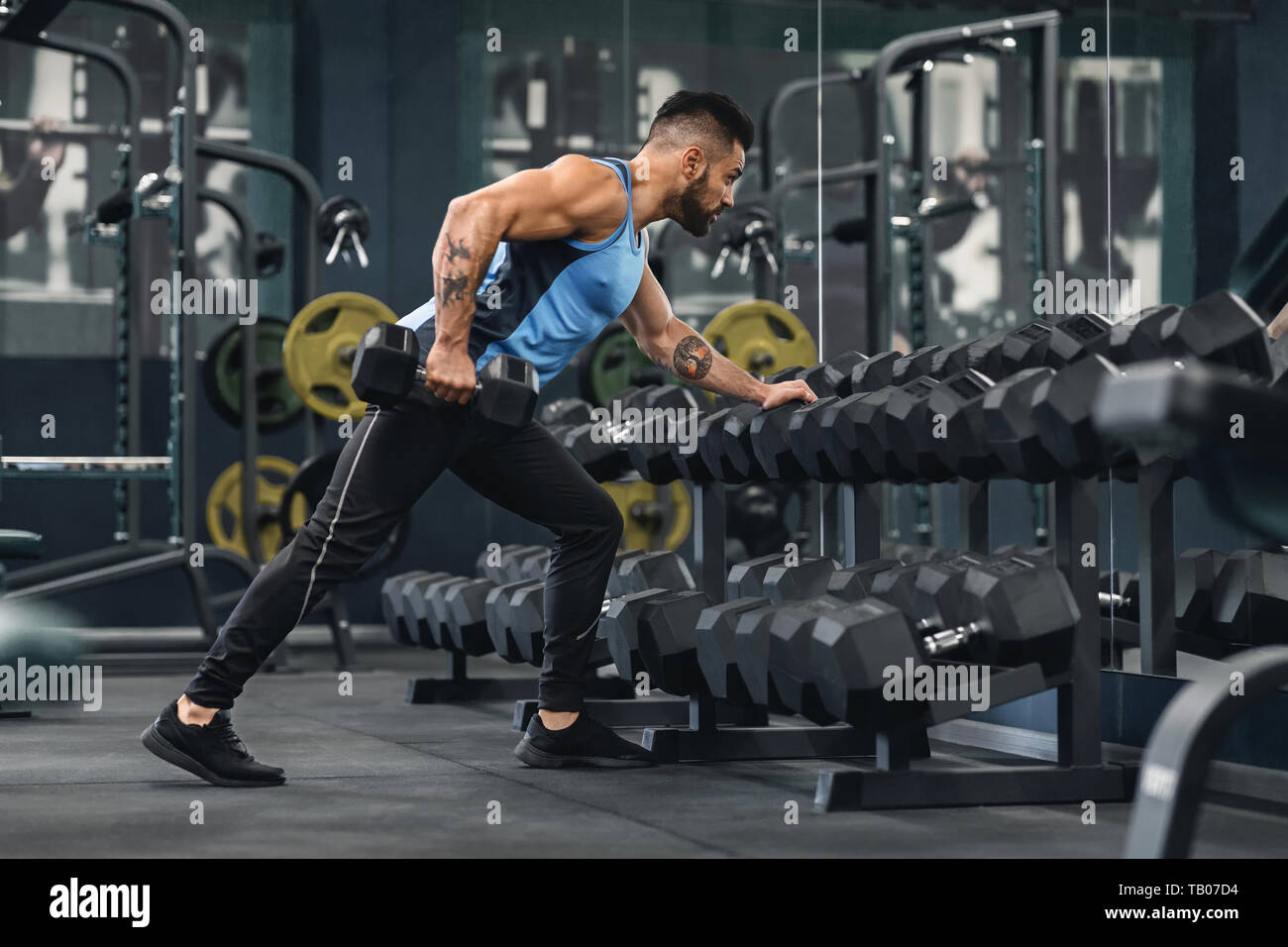 Giovani bodybuilder tenendo manubri da rack apparecchiature in palestra Foto Stock
