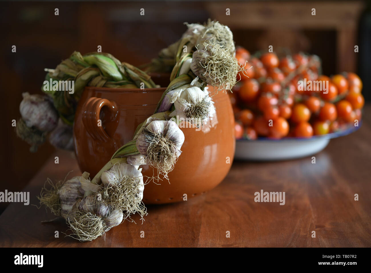 Vita Tranquilla con l'aglio, il pomodoro e la pentola di creta su un tavolo in legno in stile country Foto Stock