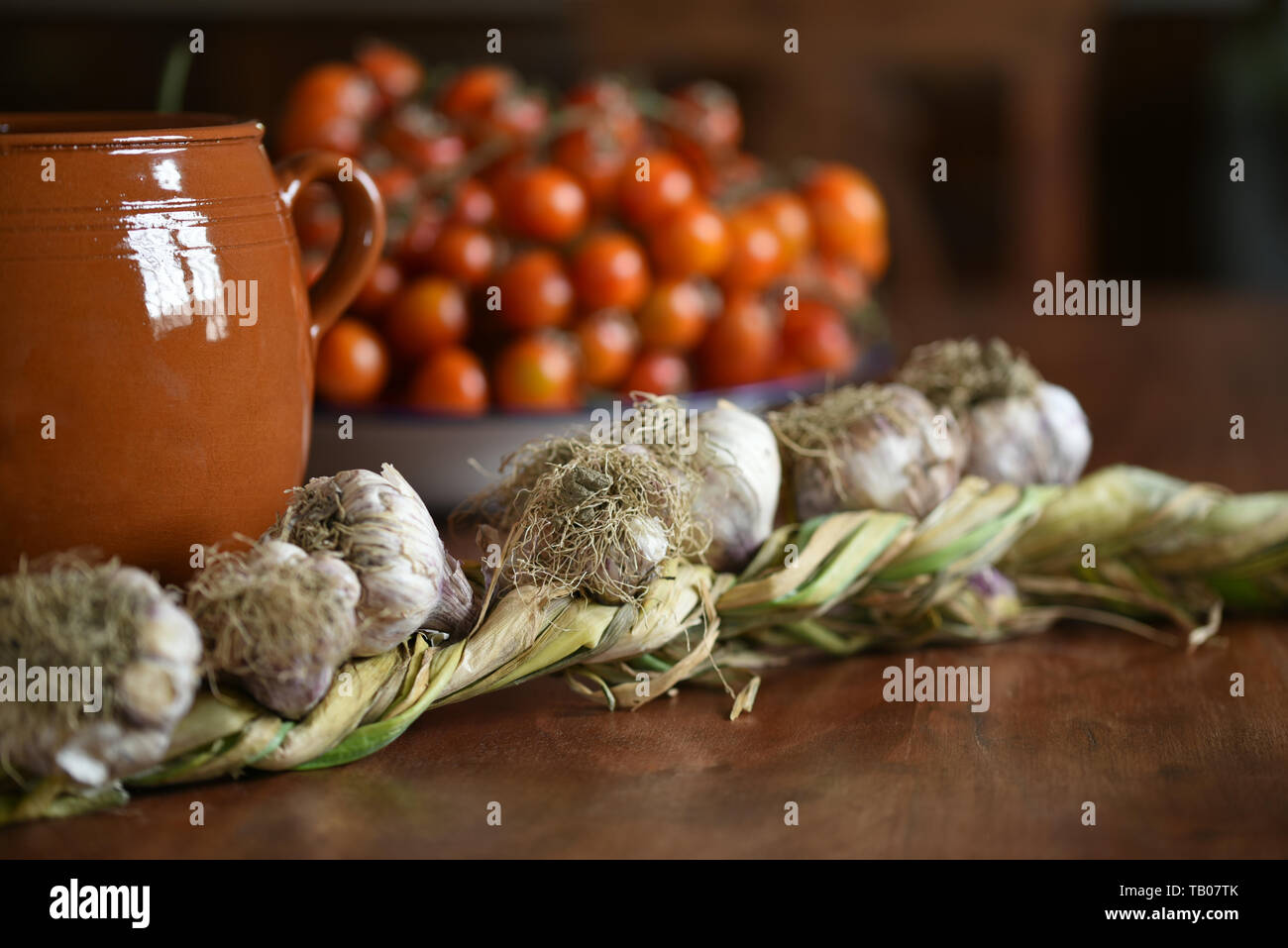 Vita Tranquilla con l'aglio, il pomodoro e la pentola di creta su un tavolo in legno in stile country Foto Stock